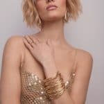 Fashion model with blonde wavy bob hairstyle and gold accessories.